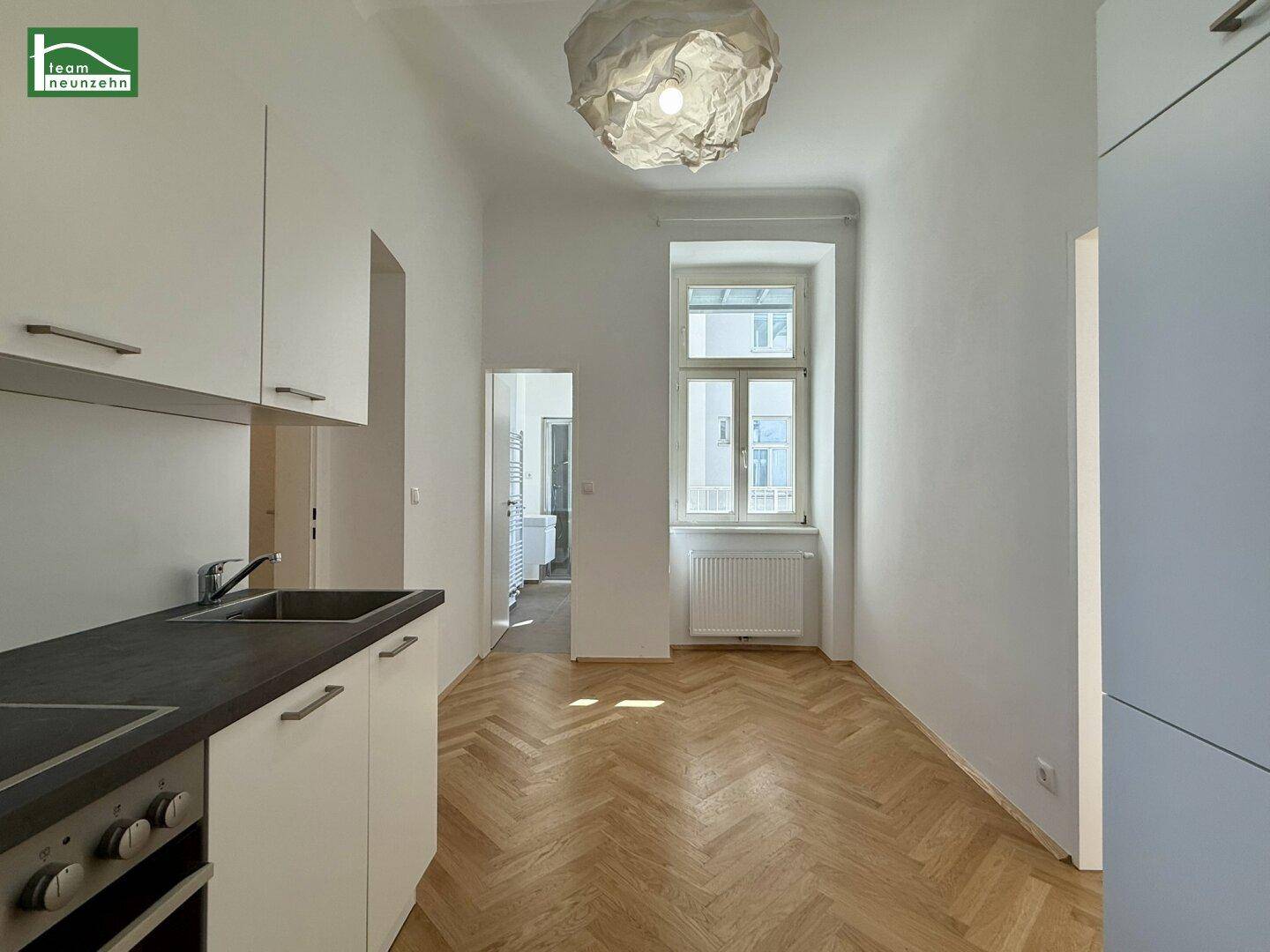 Moderne Küchenzeile mit weißen Schränken, dunkler Arbeitsplatte und Fischgrätparkett, mit Fensterblick.