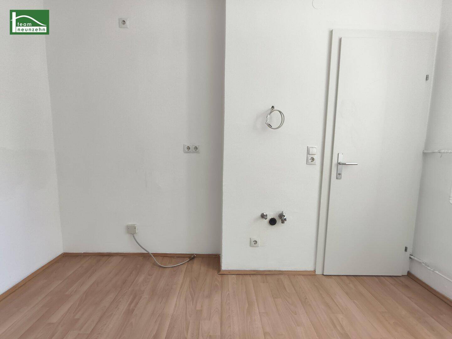 Raum mit Laminatboden und Anschlüssen für Waschmaschine oder eine kleine Küchenzeile, vielseitig nutzbar.