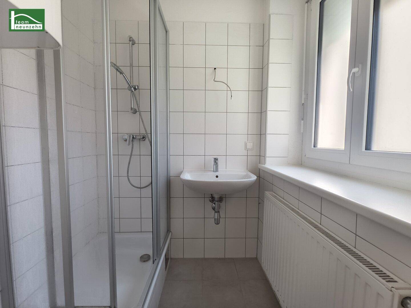 Funktionales Badezimmer mit weißen Fliesen, Duschkabine, Waschbecken und Fenster für natürliche Belüftung.