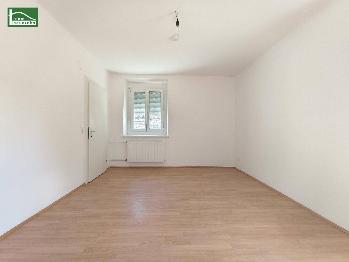 Helles Zimmer mit Laminatboden, weißen Wänden und einem Fenster mit geschlossenen Rollläden, das Privatsphäre bietet.