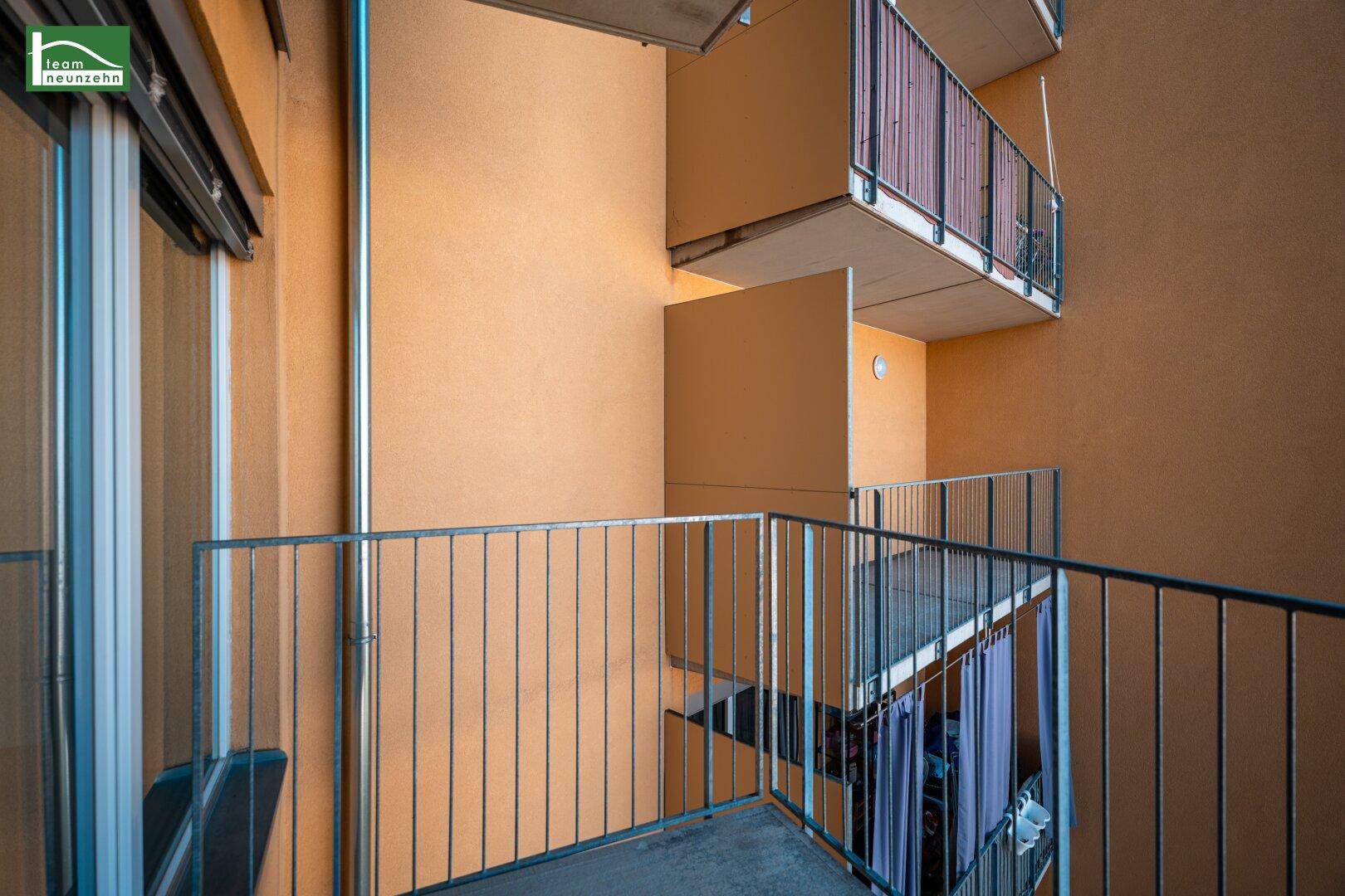 Blick vom Balkon in einen hellen Innenhof mit weiteren Balkonen und Gebäudestrukturen.