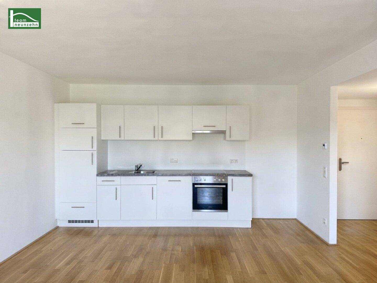 Moderne Küchenzeile mit weißen Schränken, integriertem Backofen und Dunstabzugshaube.