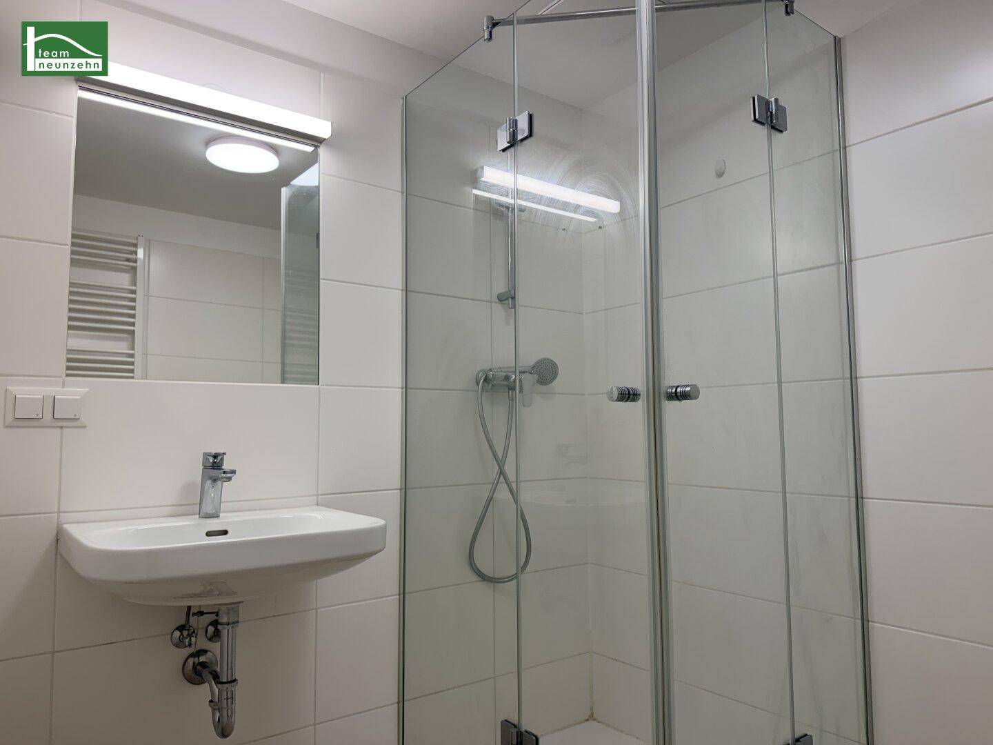Modernes Badezimmer mit weißen Fliesen, Einzelwaschbecken und einer Glasduschkabine.
