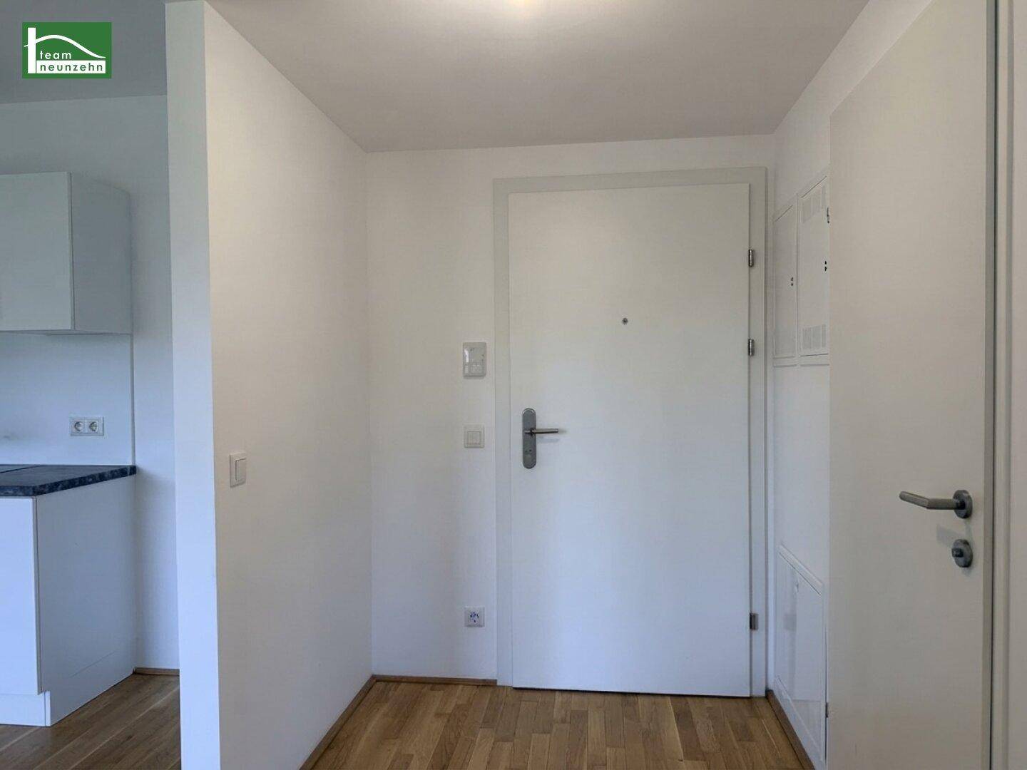Heller Eingangsbereich mit Parkettboden und weißer Eingangstür, angrenzend an den Wohnbereich.