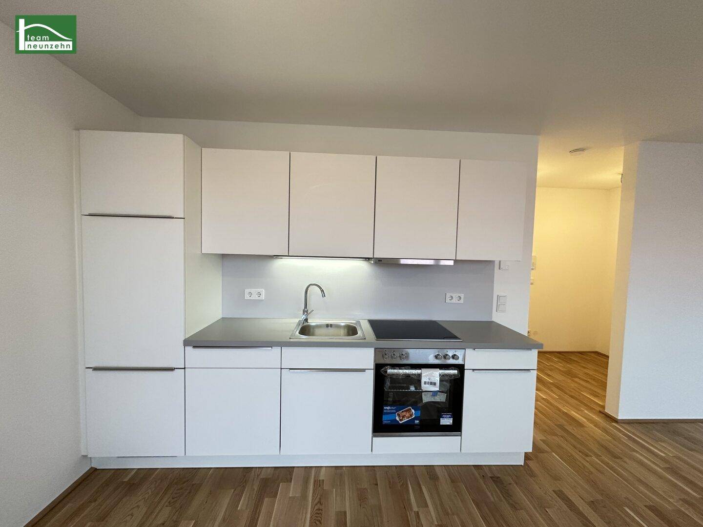 Moderne Einbauküche mit weißen Hochglanzfronten, Spüle und integriertem Backofen.