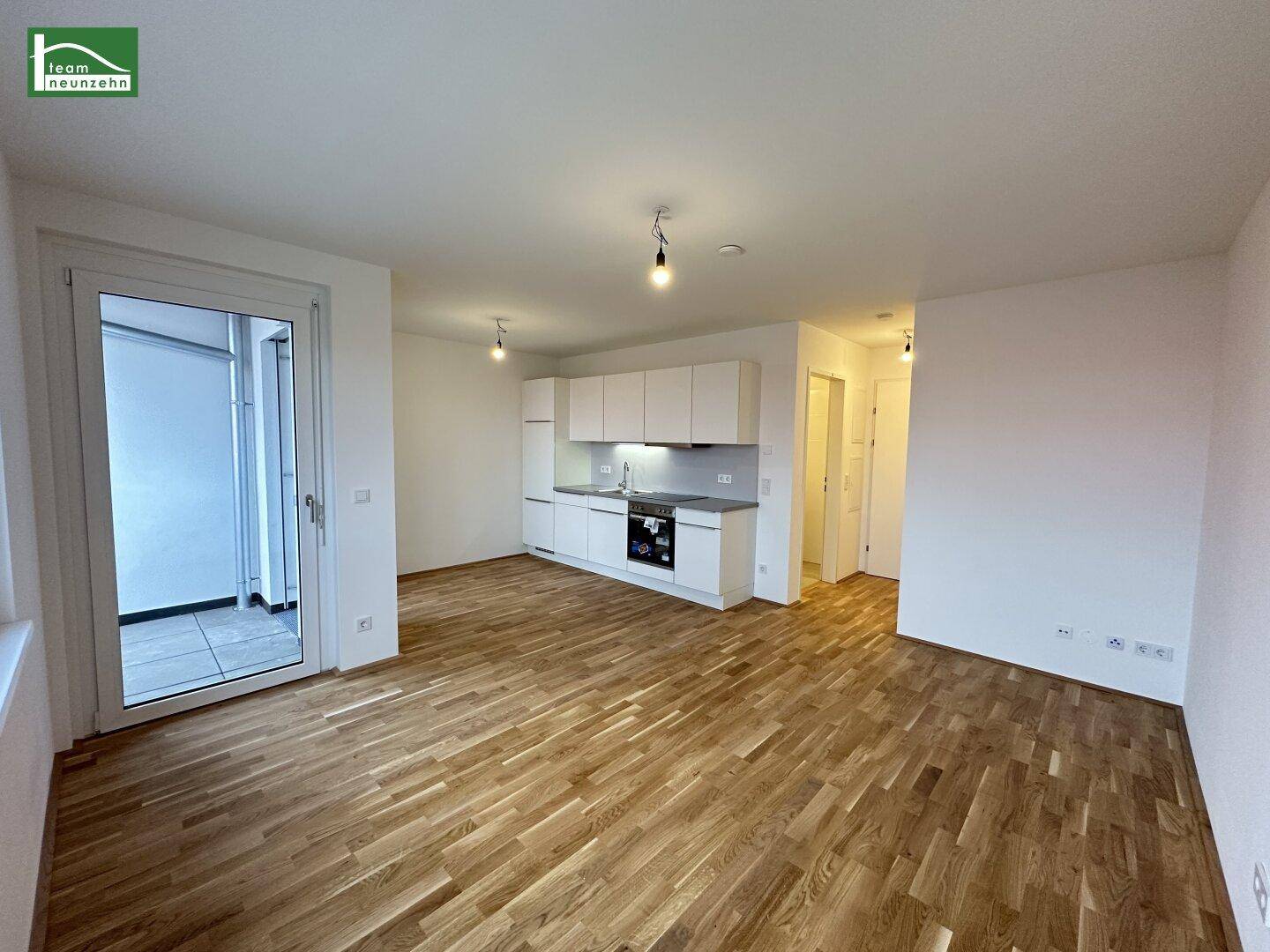 Geräumiger offener Wohnbereich mit integrierter Küche, Holzboden und Zugang zum Balkon.