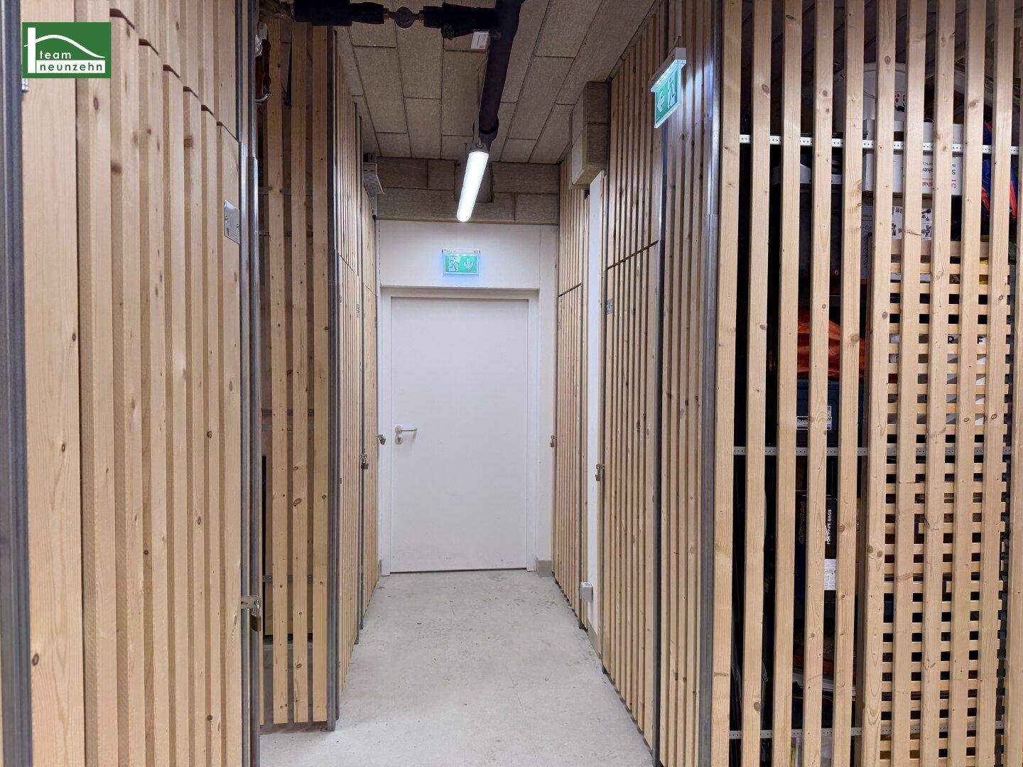Gang im Kellerbereich mit individuellen Holzlatten-Abteilen für zusätzlichen Stauraum.
