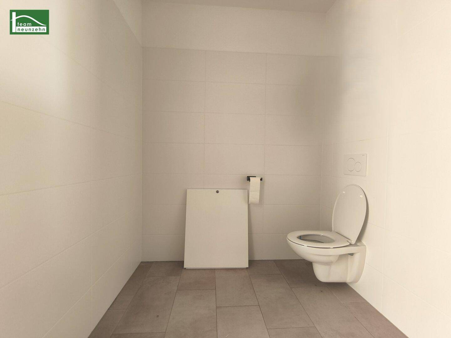 Separates WC mit wandhängender Toilette und hellen Fliesen, bietet zusätzliche Privatsphäre.