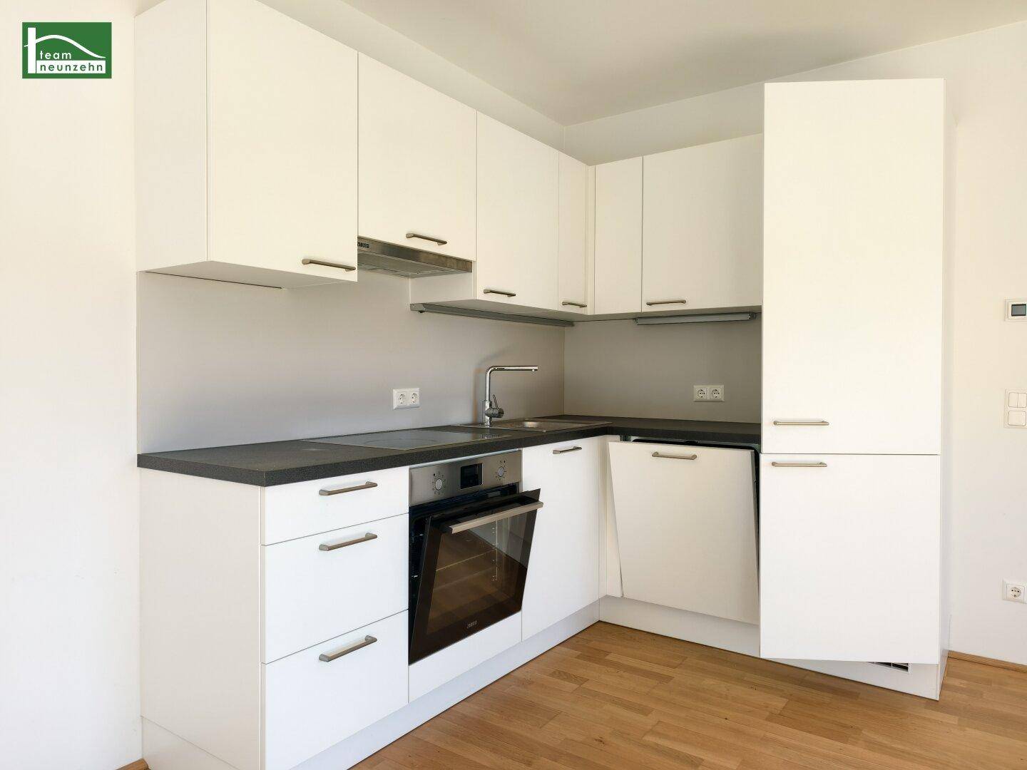 Moderne Einbauküche mit weißen Schränken, dunkler Arbeitsplatte und integrierten Geräten in neuwertigem Zustand.