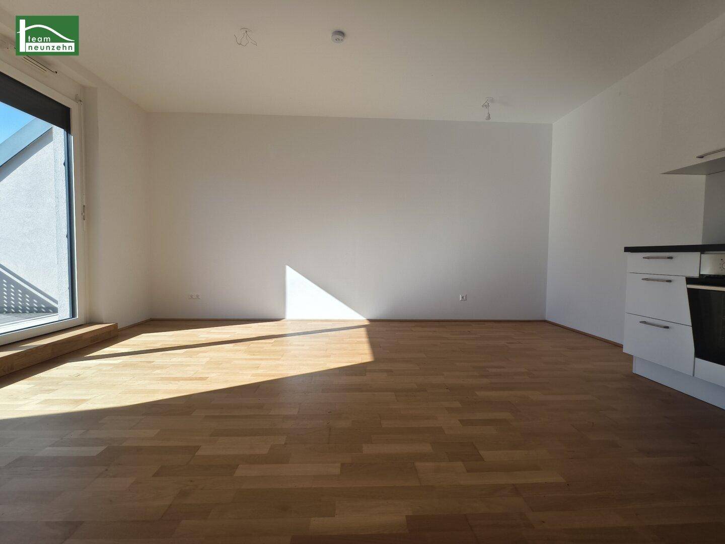 Lichtdurchfluteter Wohnbereich mit großen Fenstern und Zugang zu einem Außenbereich, ausgestattet mit Holzparkett.