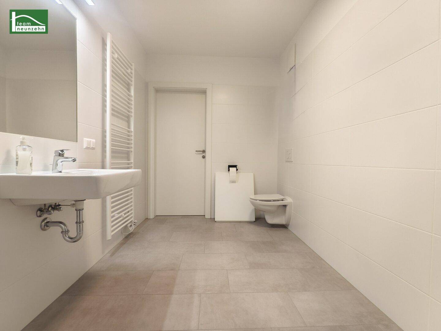 Modernes Badezimmer mit Wand-WC, Waschbecken und beheiztem Handtuchhalter, in hellen Tönen gehalten.