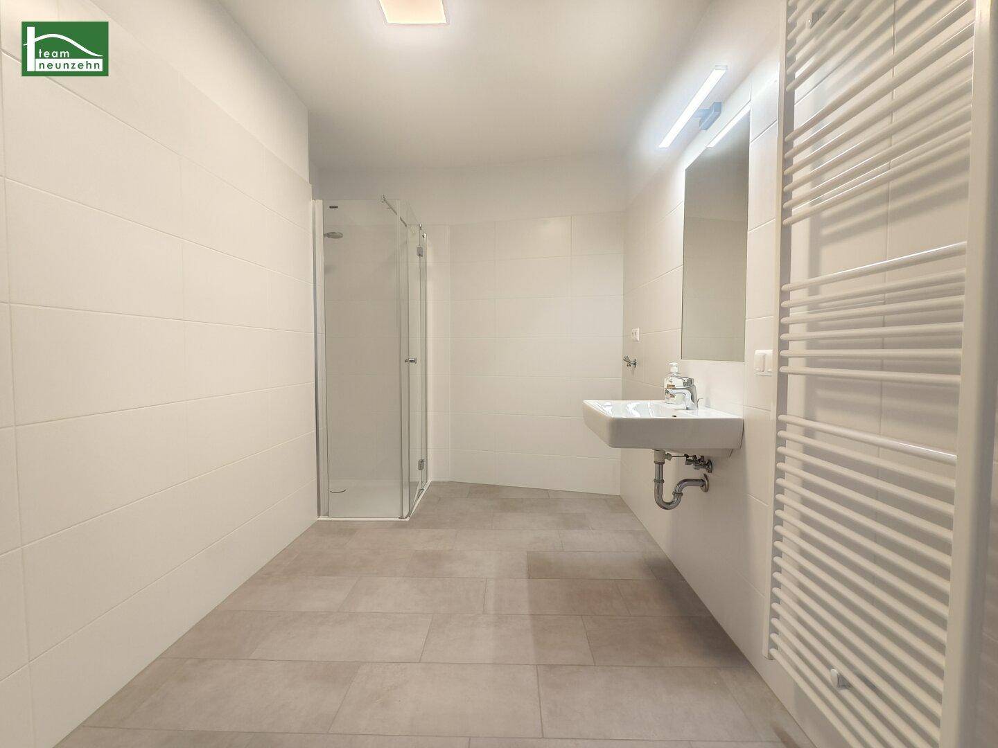Geräumiges Badezimmer mit ebenerdiger Dusche, Waschbecken und Handtuchheizkörper, in modernem Design.