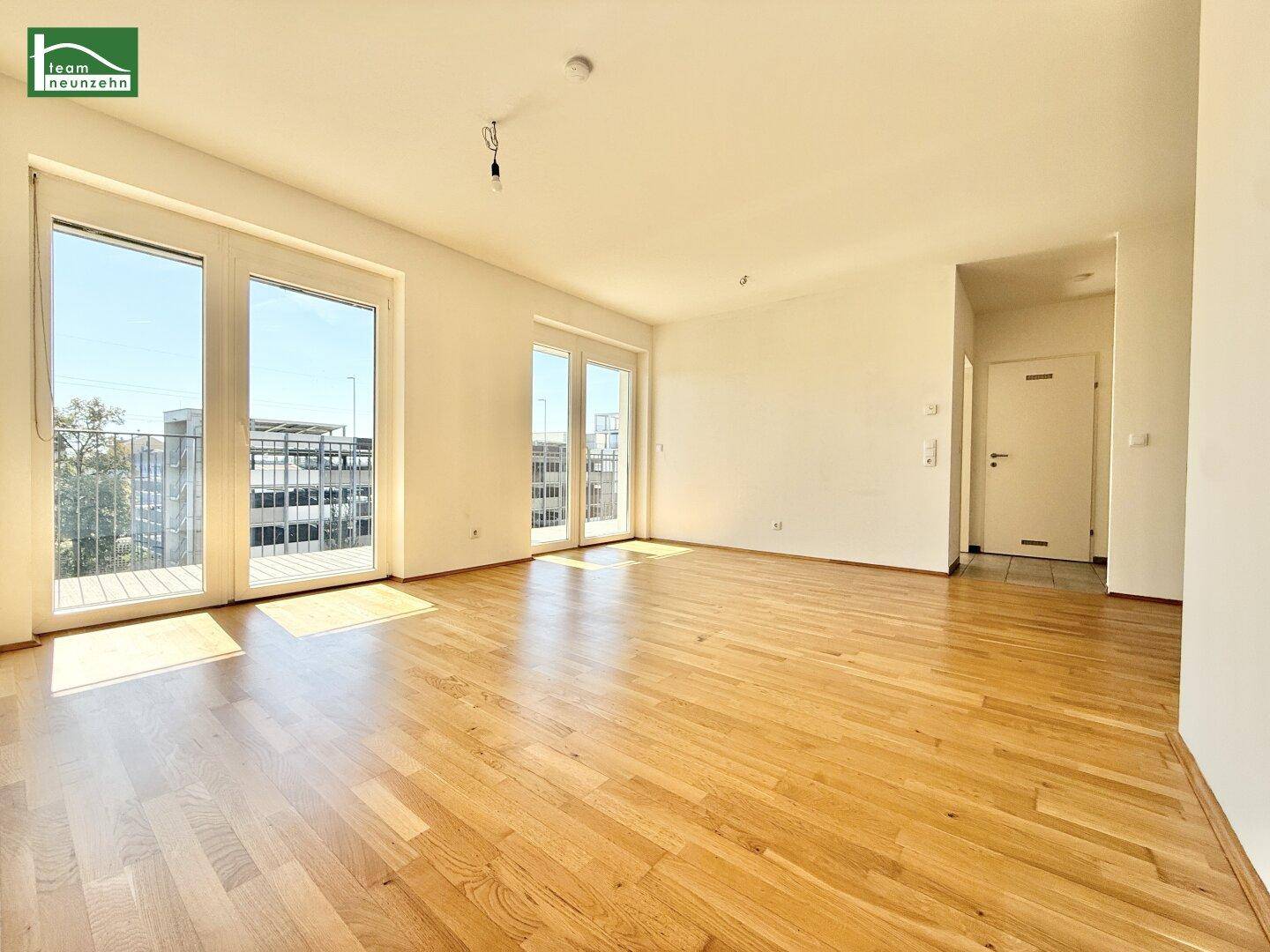 Geräumiges Wohnzimmer mit Parkettboden und zwei großen Balkonzugängen, die viel Licht hereinlassen.