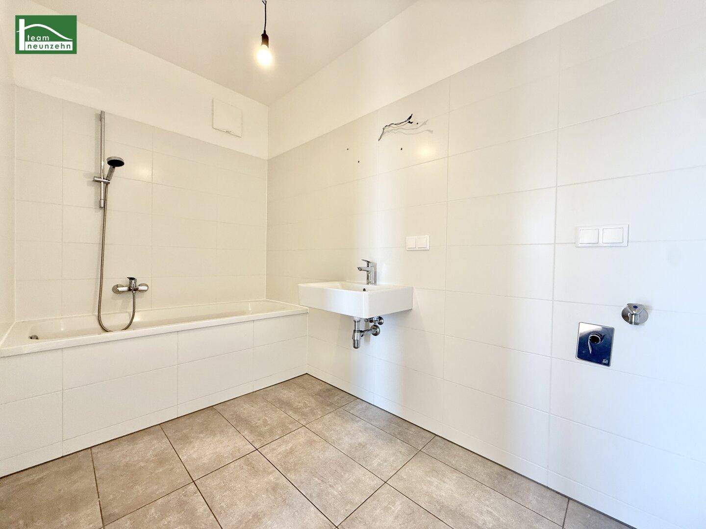 Modernes Badezimmer mit Badewanne, Duschfunktion, Einzelwaschbecken und hellen Fliesen.