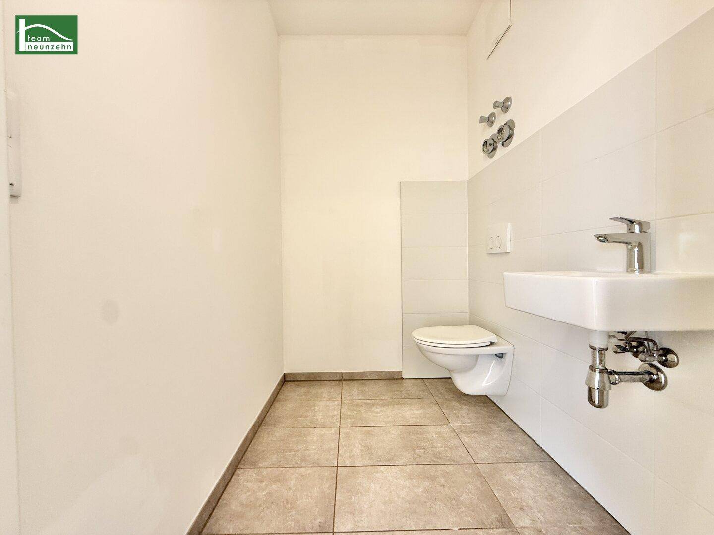 Separates WC mit wandhängender Toilette, kleinem Waschbecken und modernen Fliesen.