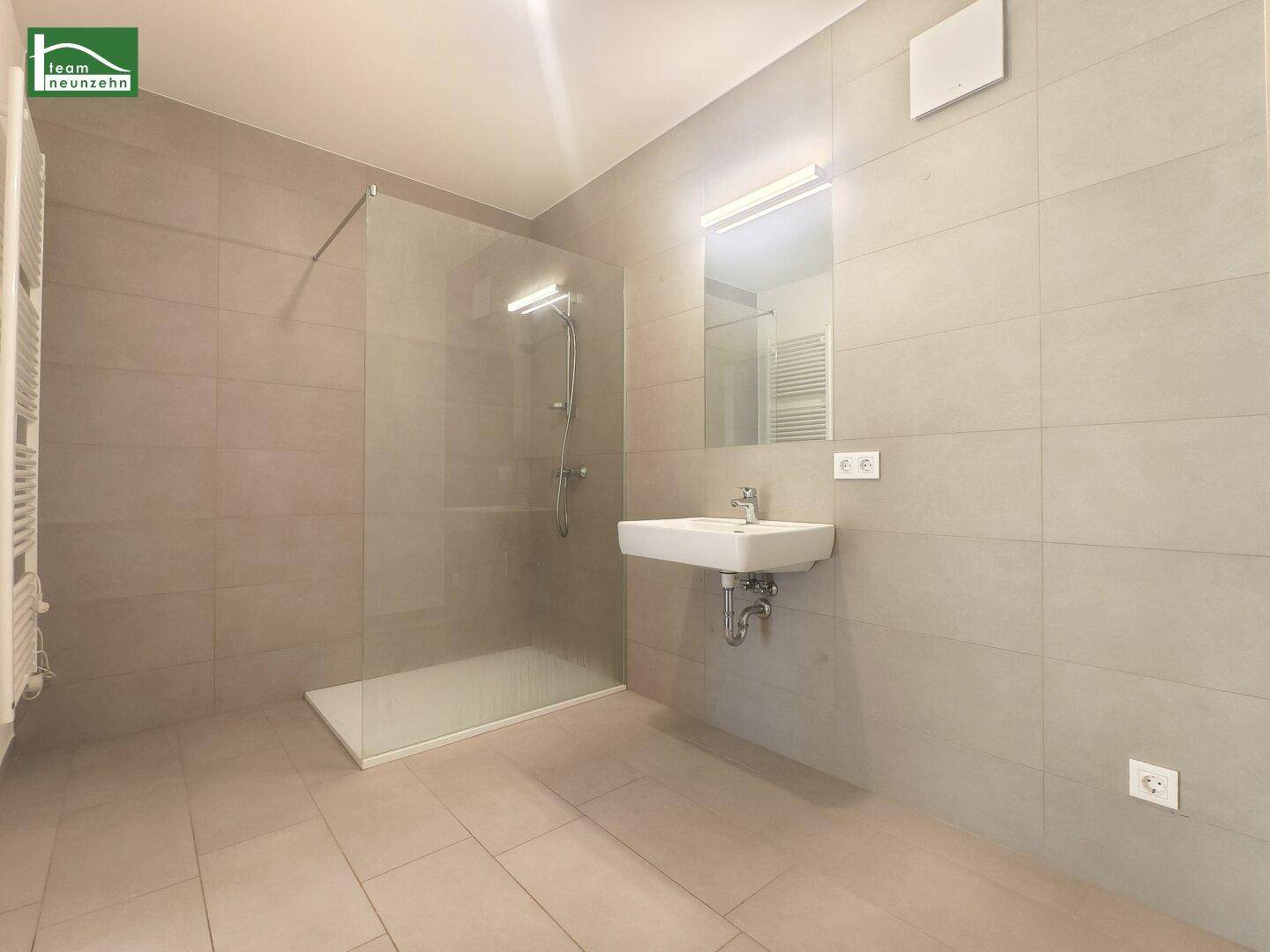Modernes Badezimmer mit ebenerdiger Dusche, eleganten Fliesen und Waschtisch.