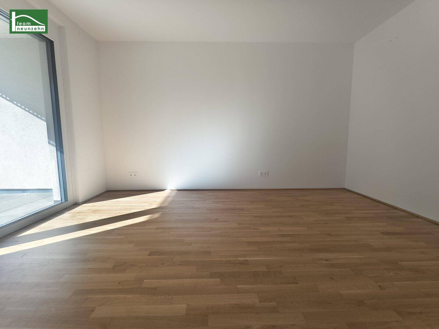 Heller Raum mit Holzboden und großem Fenster, das viel Tageslicht hereinlässt.