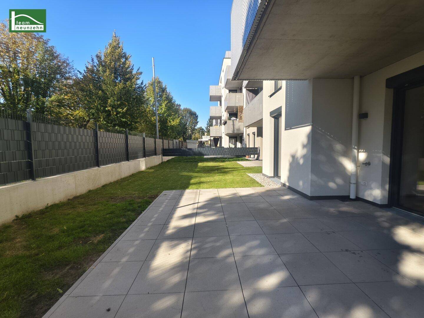 Lange Terrasse mit angrenzendem Rasenbereich und blickdichtem Zaun.