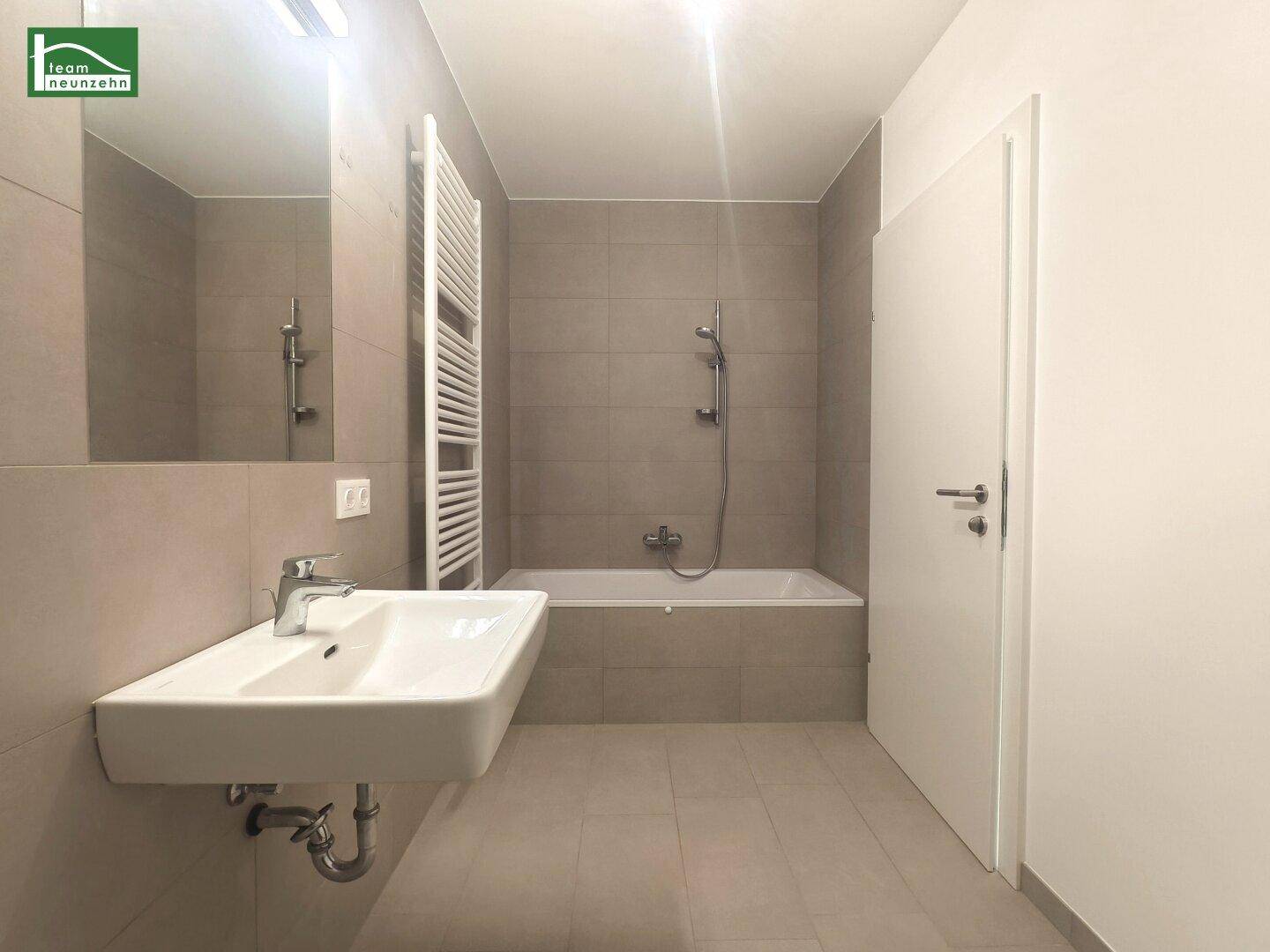 Modernes Badezimmer mit Badewanne, Waschtisch und beheiztem Handtuchhalter.