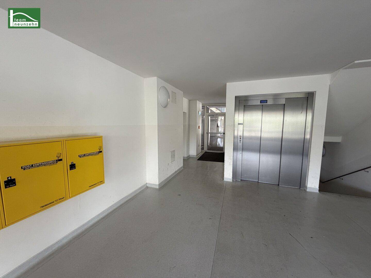 Heller Flur im Eingangsbereich eines Gebäudes mit Aufzug und gelben Briefkästen.