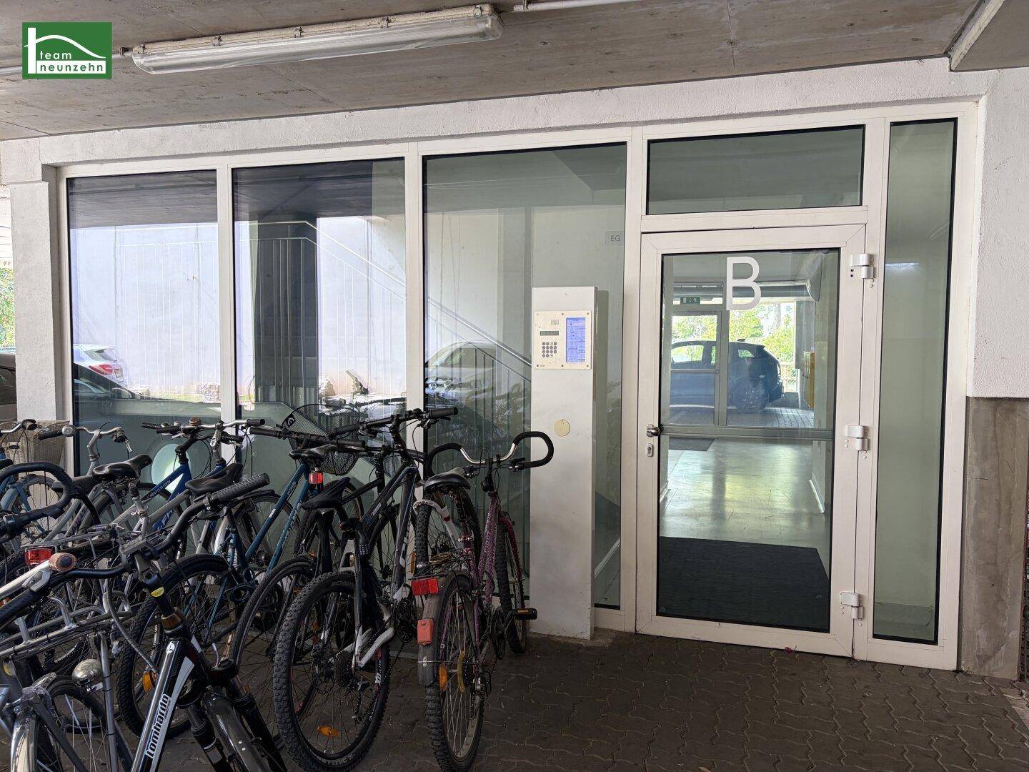 Eingangsbereich eines Gebäudes mit vielen abgestellten Fahrrädern und einer Glastür.