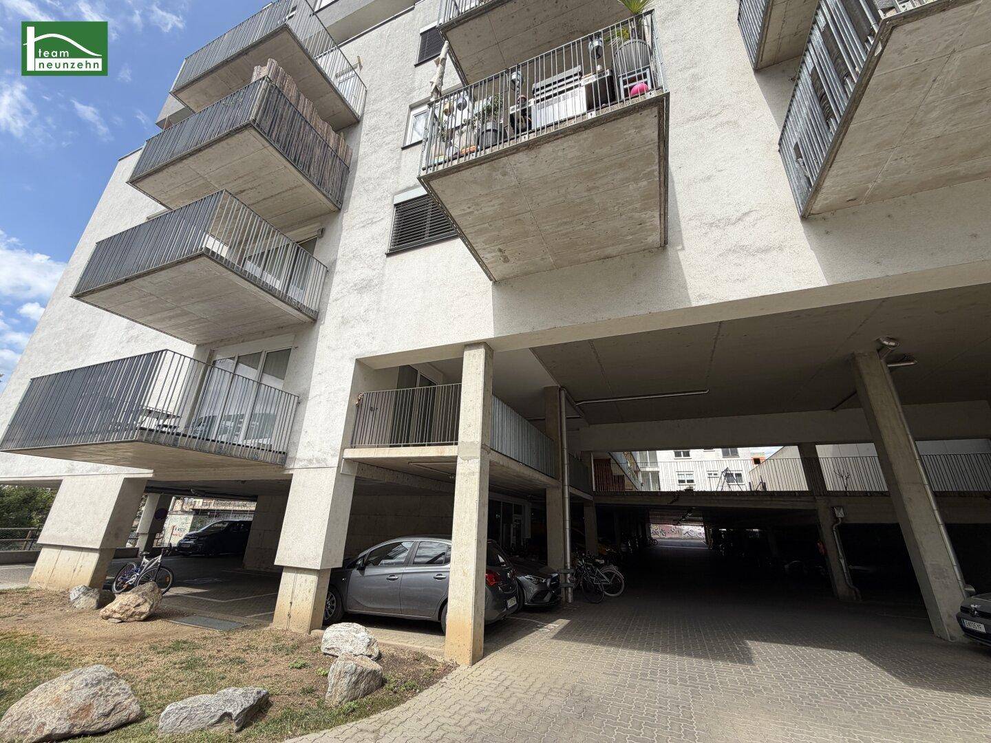 Moderne Wohnhausfassade mit mehreren Balkonen und überdachten Parkplätzen im Erdgeschoss.