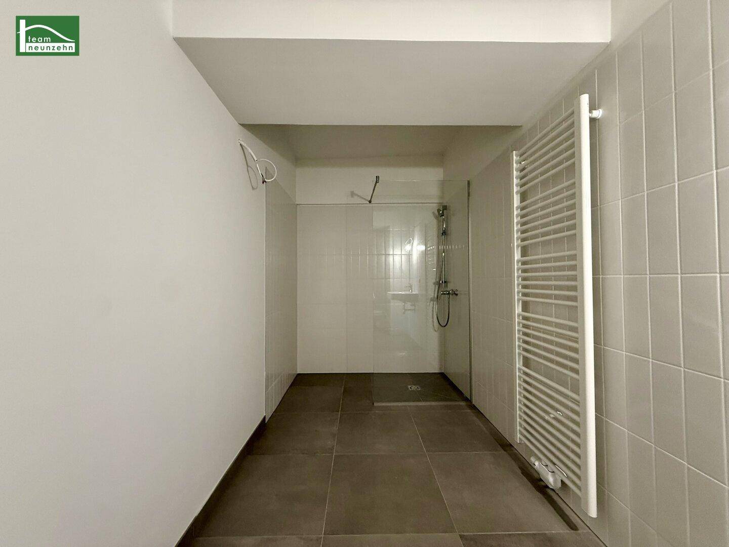 Modernes Badezimmer mit ebenerdiger Dusche, weißen Fliesen und Handtuchheizkörper.