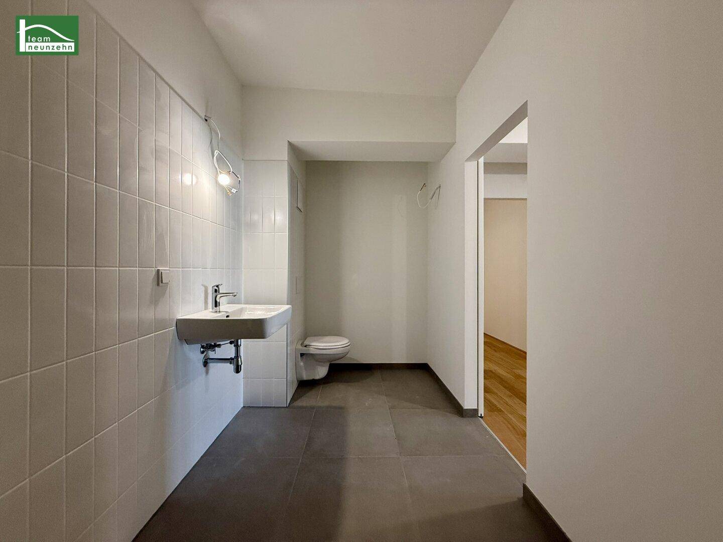 Badezimmer mit Waschbecken und Toilette, komplett gefliest in hellen Farben.