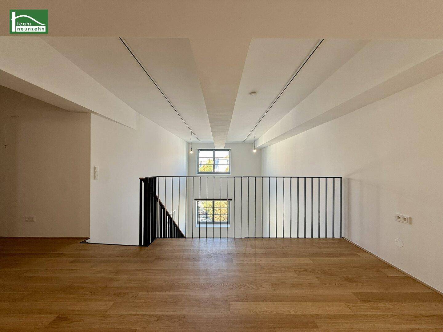 Galerie mit Holzboden und Blick auf den darunterliegenden Wohnbereich mit hohen Fenstern.