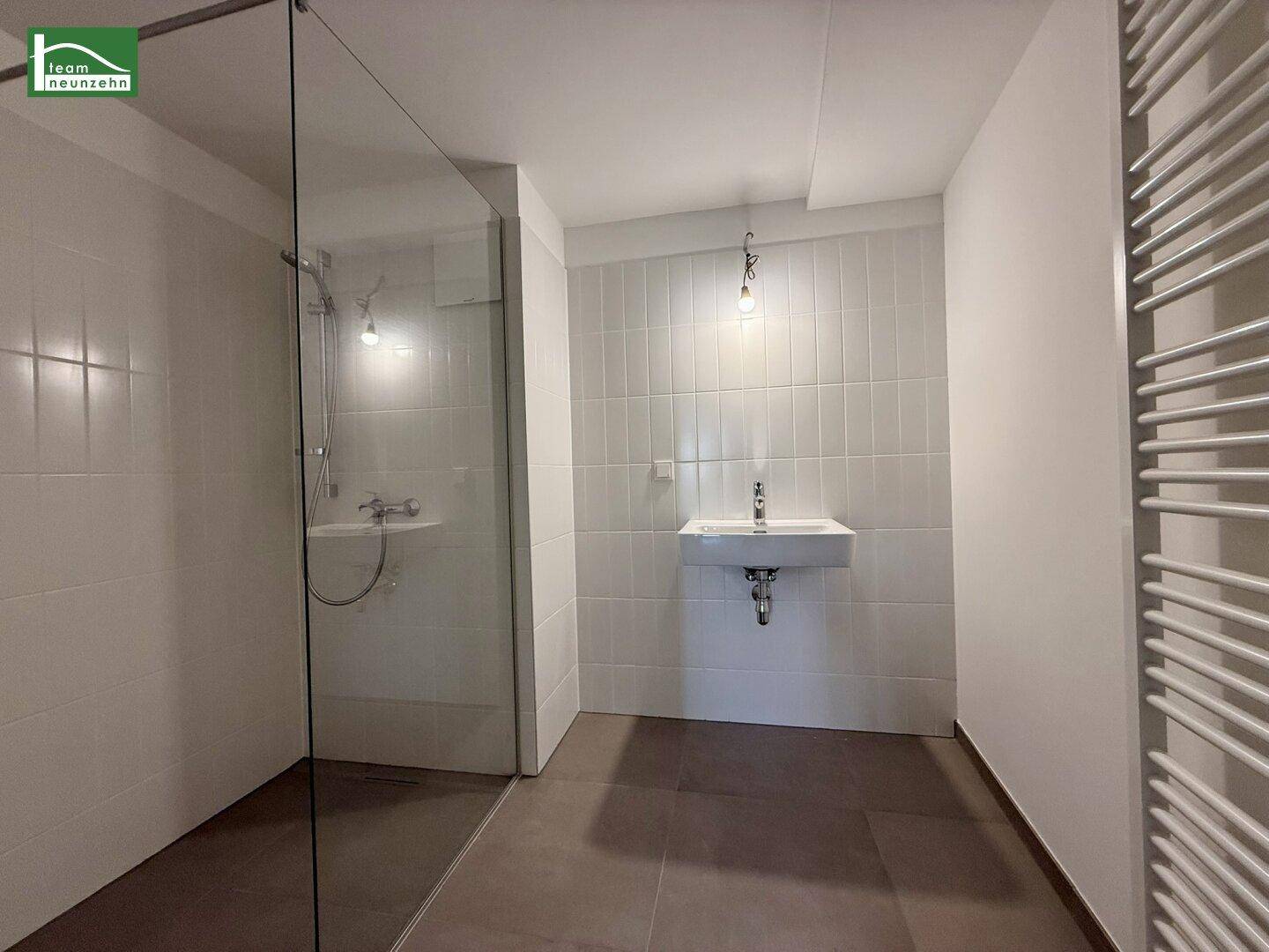 Modernes Badezimmer mit ebenerdiger Dusche, Waschbecken und Handtuchheizkörper.