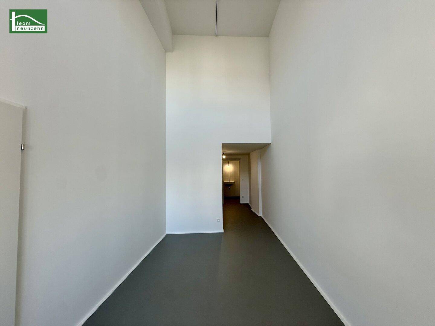 Geräumiger, heller Raum mit hoher Decke und grauem Boden, ideal für verschiedene Nutzungen.