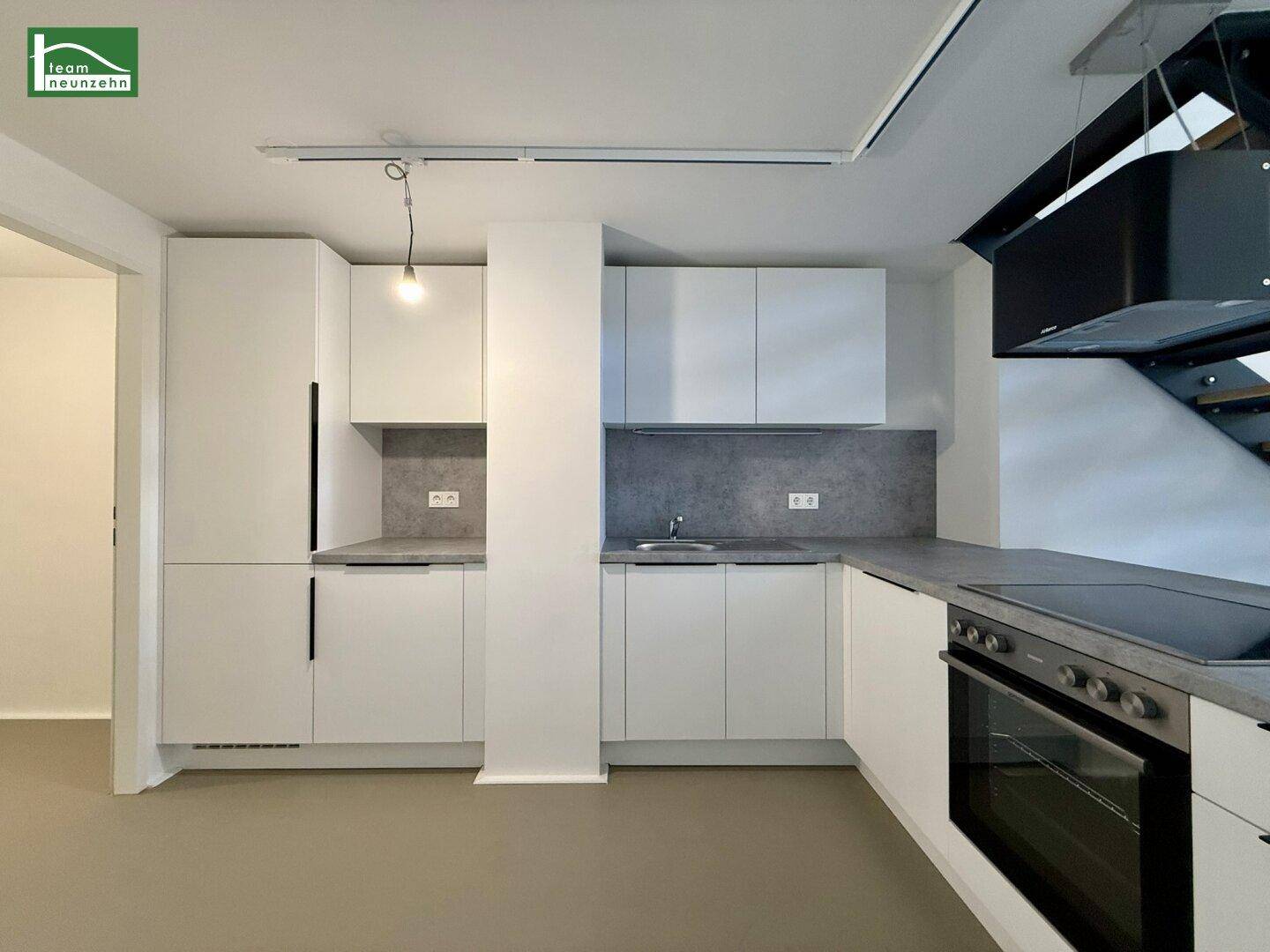 Moderne Einbauküche mit weißen Schränken, grauen Arbeitsplatten und integrierten Geräten.