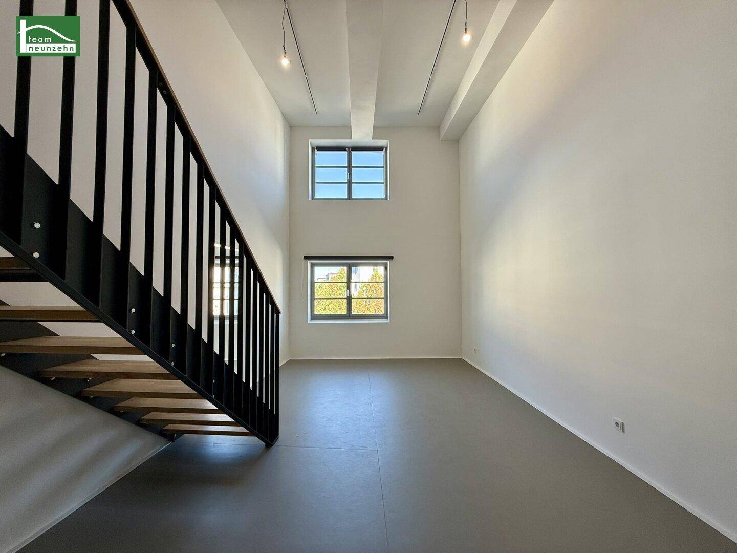 Geräumiger, heller Wohnbereich mit hohen Decken, großen Fenstern und moderner Treppe.