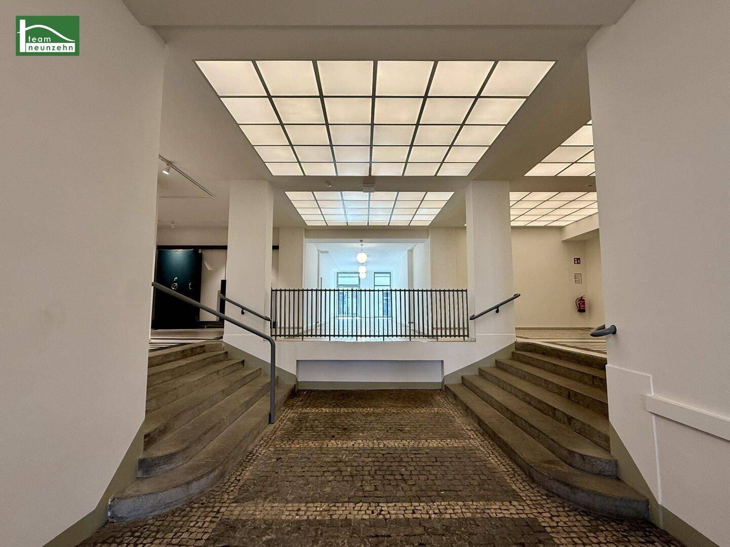 Geräumiger Flur mit Treppen, Rampe und moderner Deckenbeleuchtung, der zu weiteren Bereichen führt.