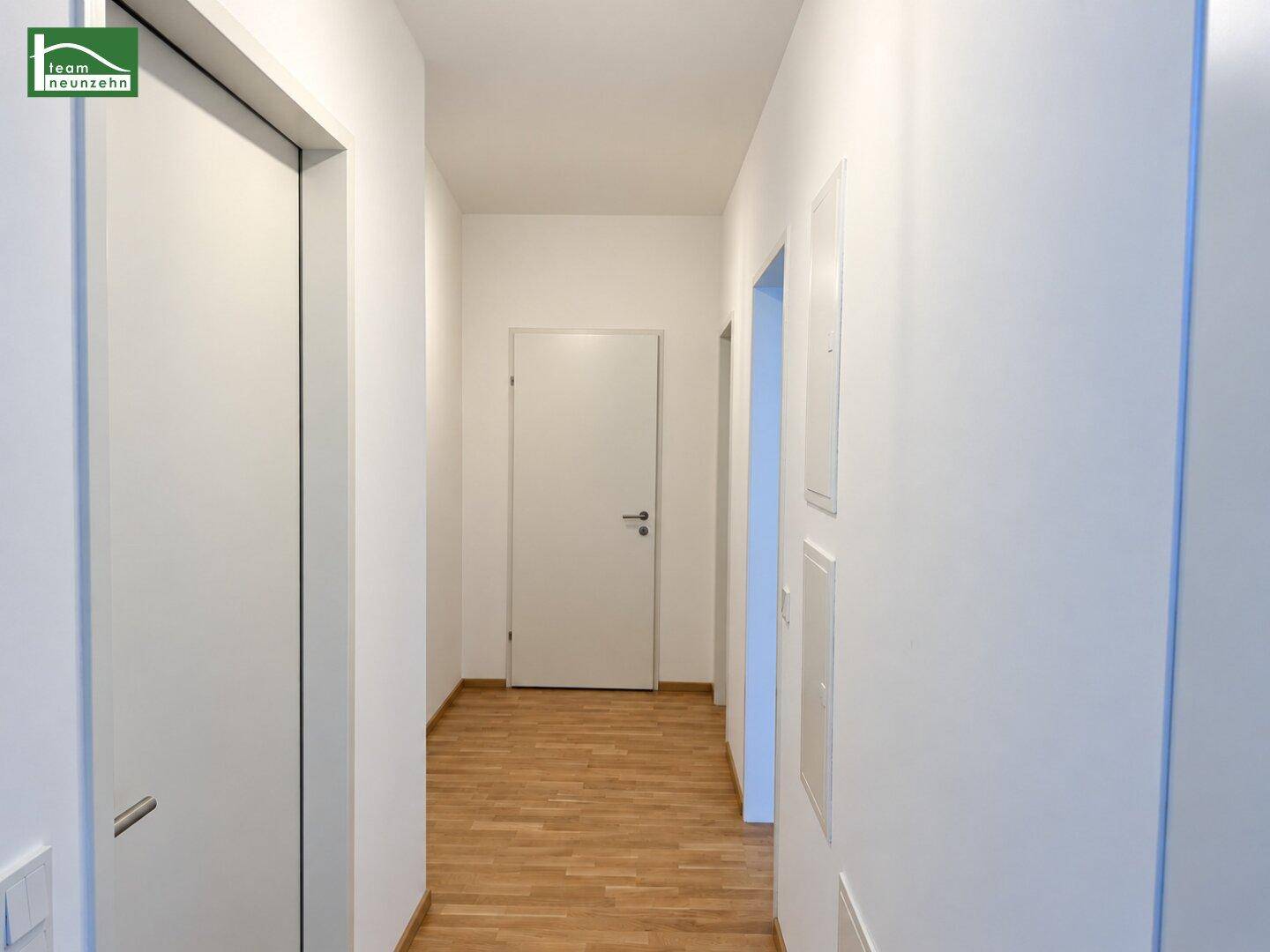 Langer, heller Flur mit Holzboden und weißen Türen, der verschiedene Räume verbindet.