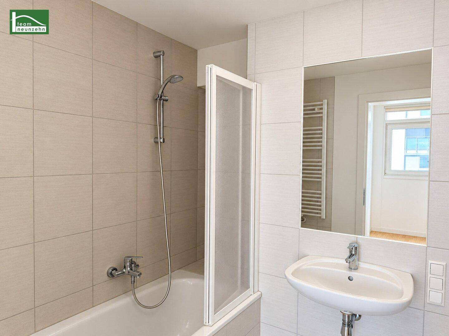 Modernes Badezimmer mit beigen Fliesen, Badewanne mit Duschfunktion und beheiztem Handtuchhalter.