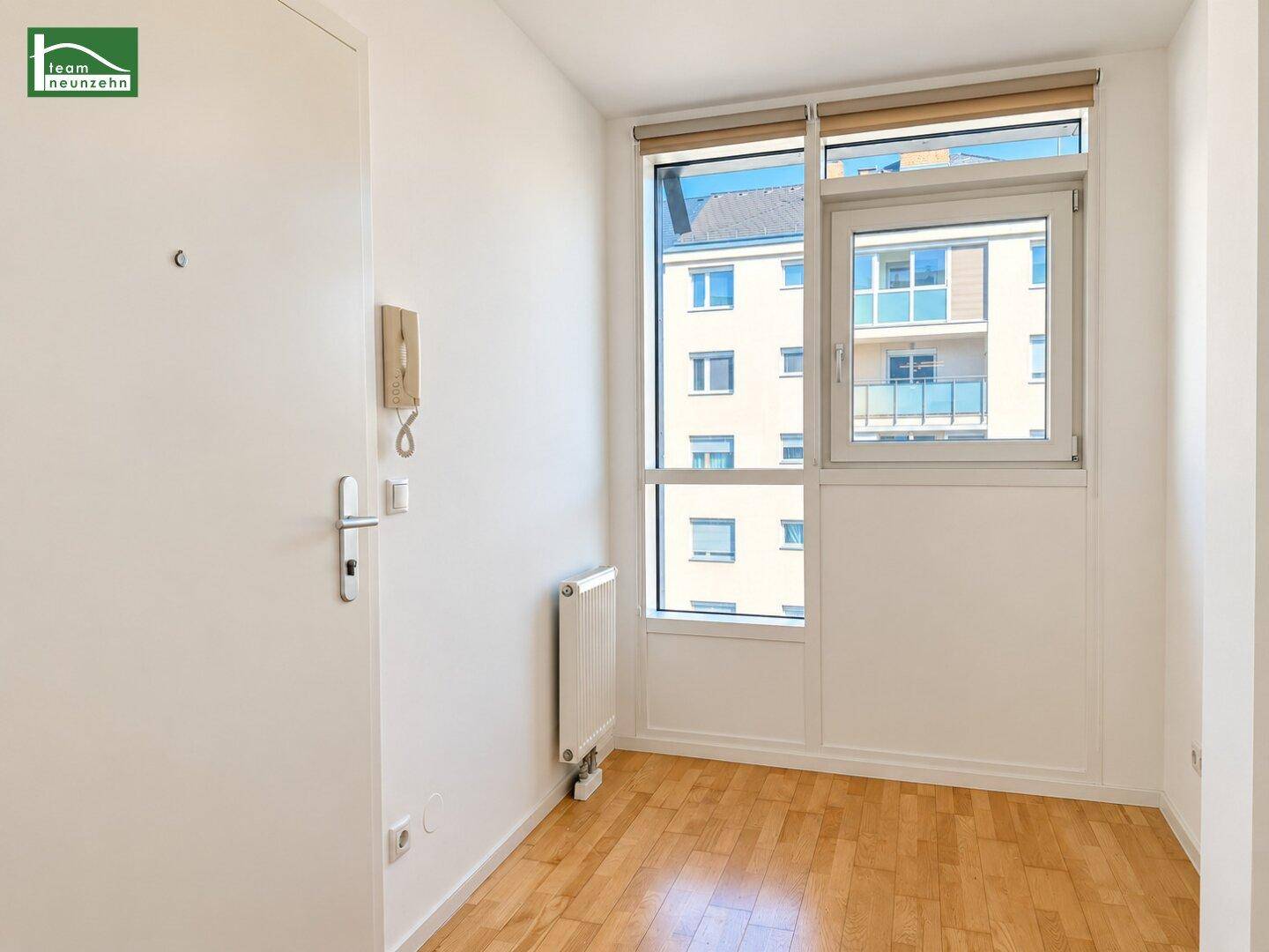 Heller Eingangsbereich mit Parkettboden, Fenster und Gegensprechanlage an der Wand.