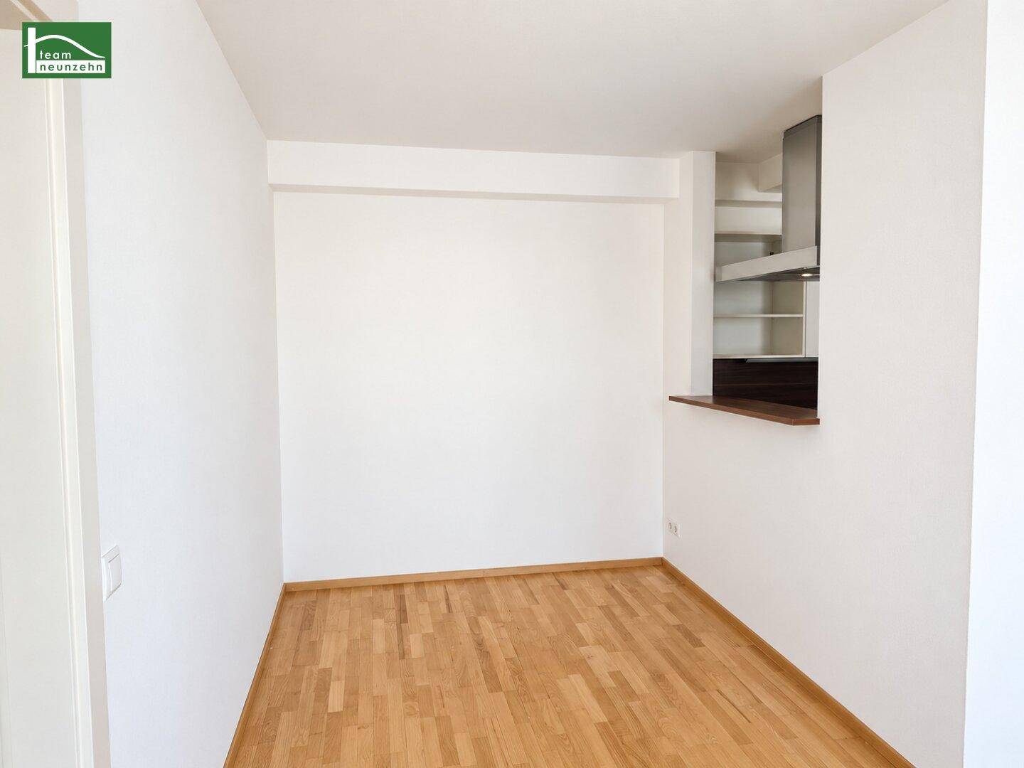 Heller Raum mit Parkettboden und vorbereiteter Ecke für eine Küchenzeile mit Dunstabzugshaube.