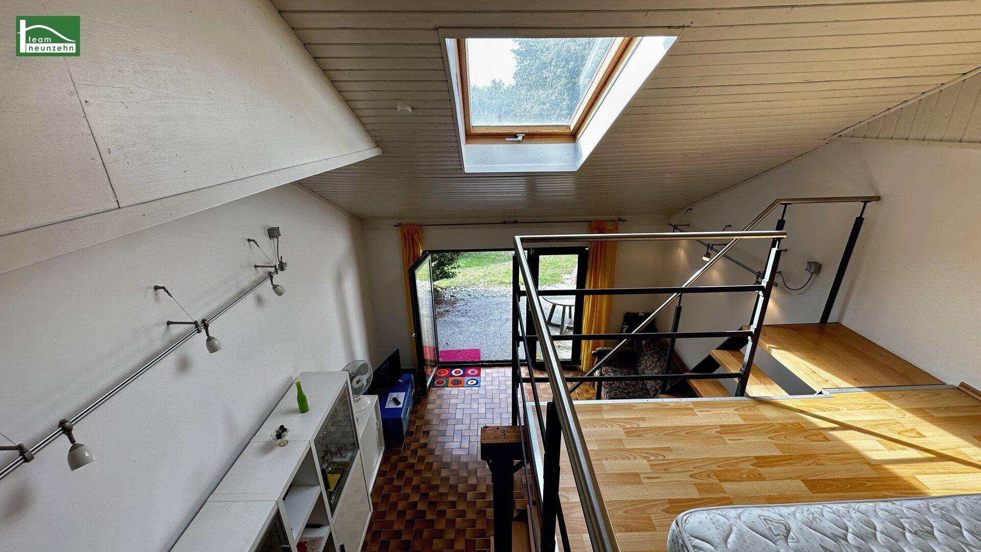 Blick von der Galerie auf den offenen Wohnbereich mit Zugang zum Garten und Dachfenster.