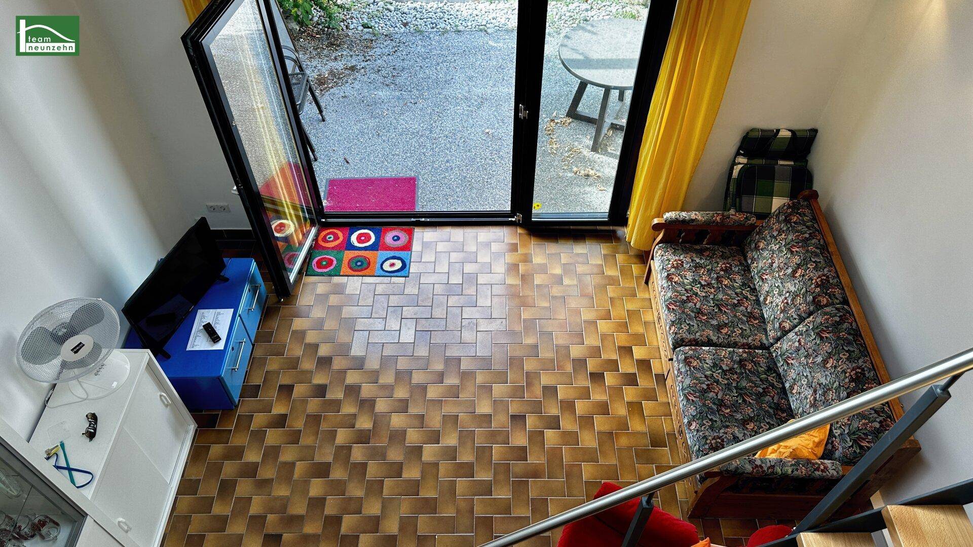 Wohnbereich mit gefliestem Boden, Sofa und Zugang zur Terrasse mit Blick ins Grüne.