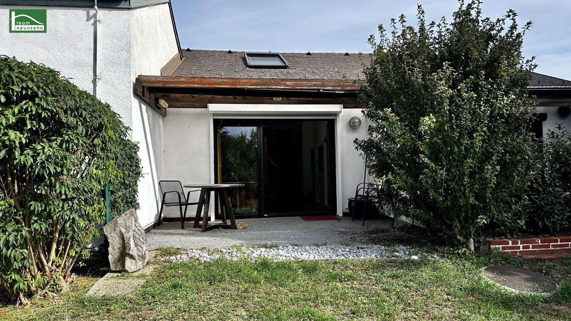 Gartenbereich mit kleiner Terrasse, Rasenfläche und Sträuchern hinter dem Haus.