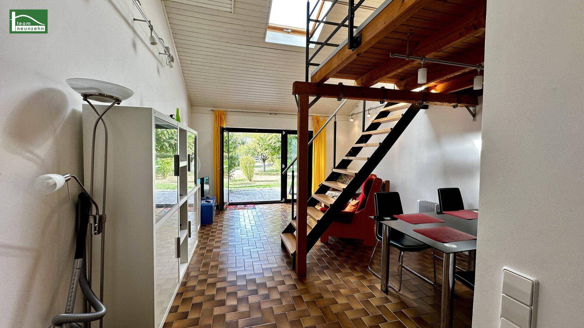Geräumiger Wohn- und Essbereich mit Holztreppe zur Galerie und Blick ins Grüne.