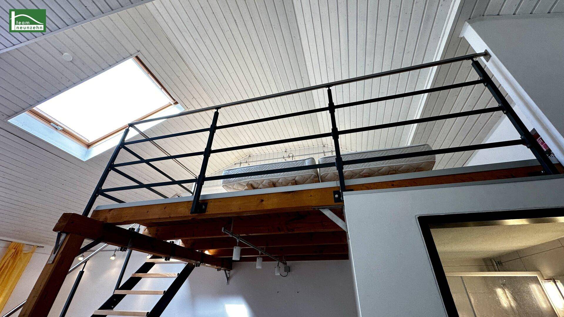 Schlafbereich auf einer Holzgalerie mit Metallgeländer und Dachfenster für natürliches Licht.