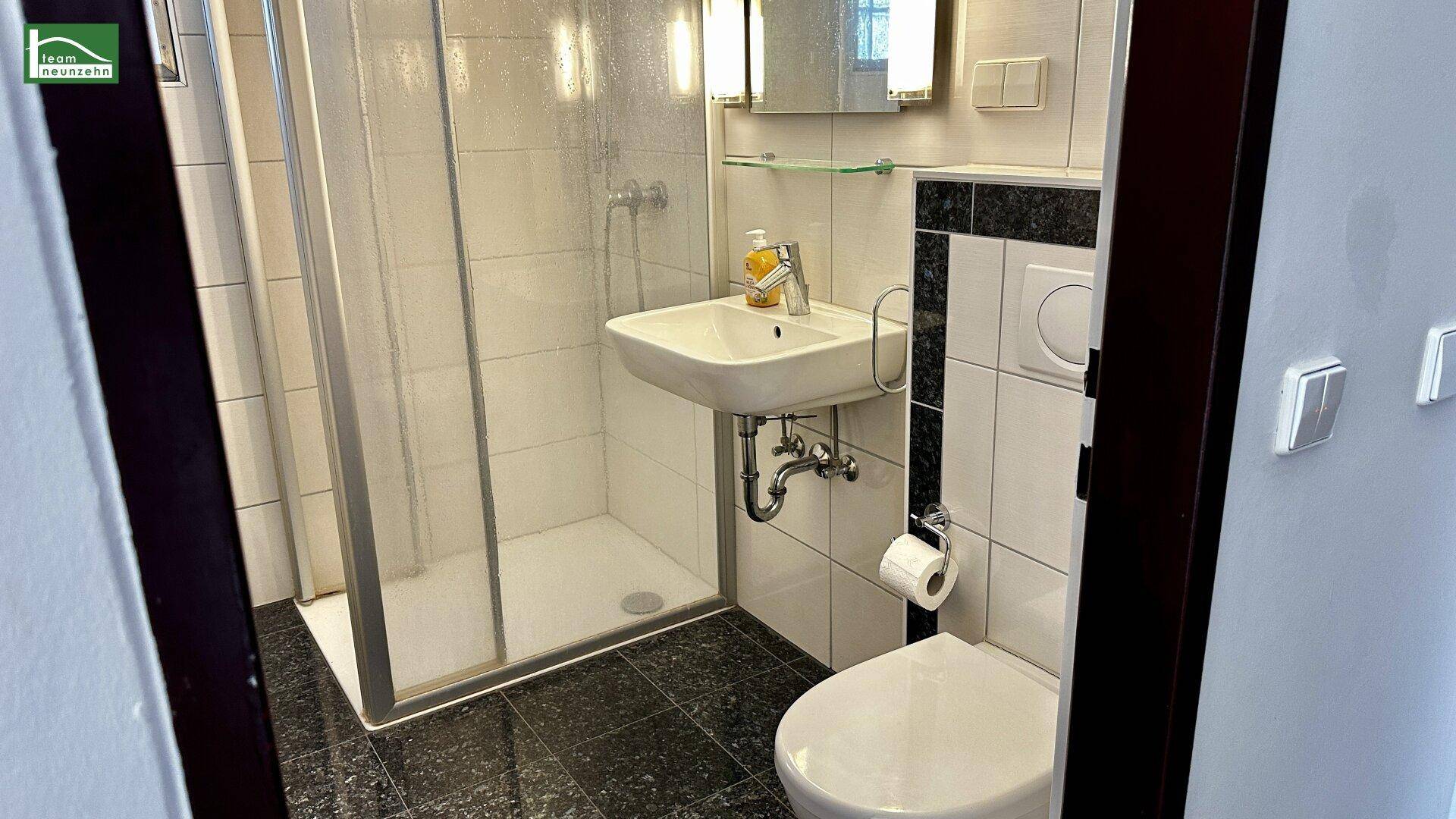 Modernes Badezimmer mit Duschkabine, wandmontierter Toilette und kleinem Waschbecken.