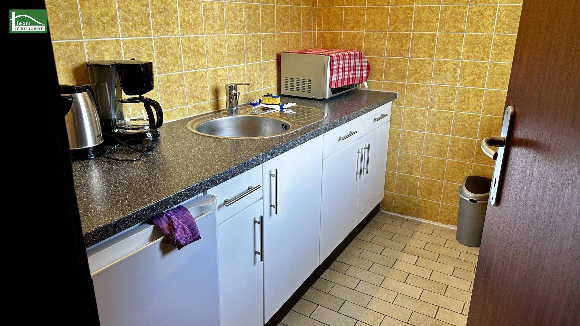 Detailansicht einer funktionalen Küchenzeile mit Spüle, Kaffeemaschine und gelben Fliesen.