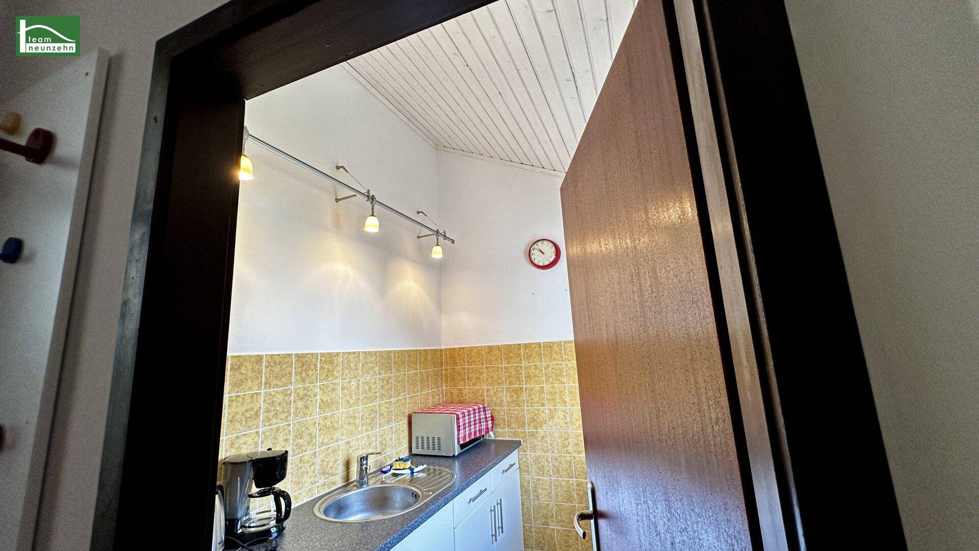 Kleine Küchenzeile mit Spüle, Kaffeemaschine und Mikrowelle, gefliesten Wänden.