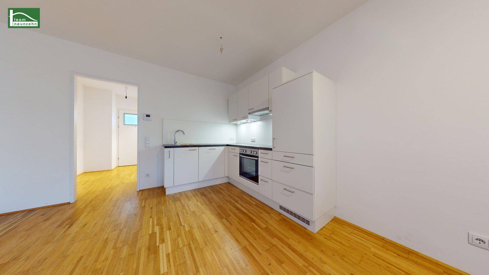 Kompakte Einbauküche mit weißen Schränken und Holzboden, offen zum Wohnbereich.