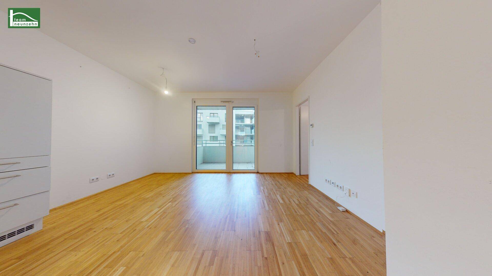 Heller Wohnbereich mit Holzboden und großen Fenstern, die Zugang zu einem Balkon bieten.