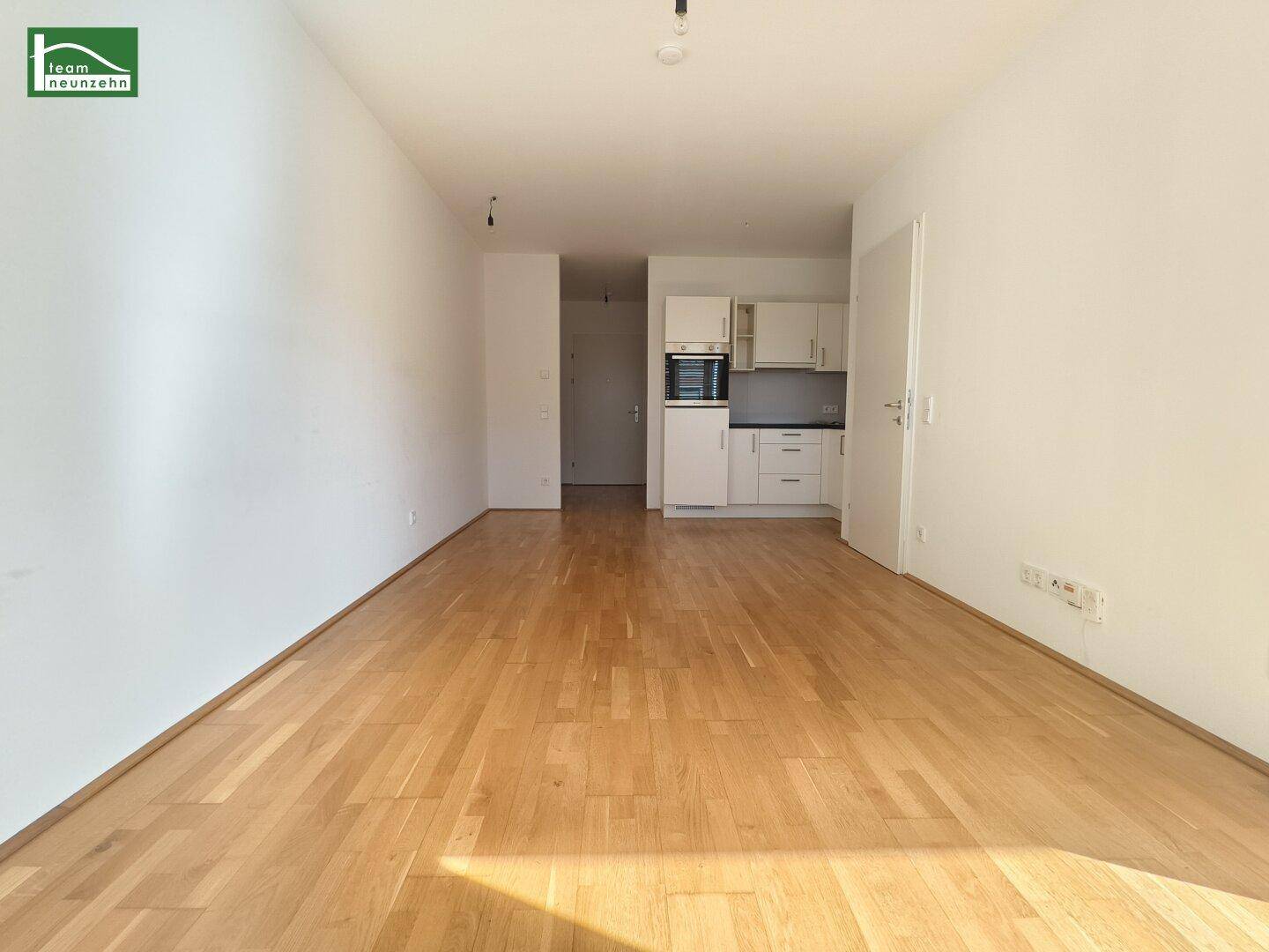 Offener Wohnbereich mit Holzboden und Blick auf die integrierte Küchenzeile im Hintergrund.