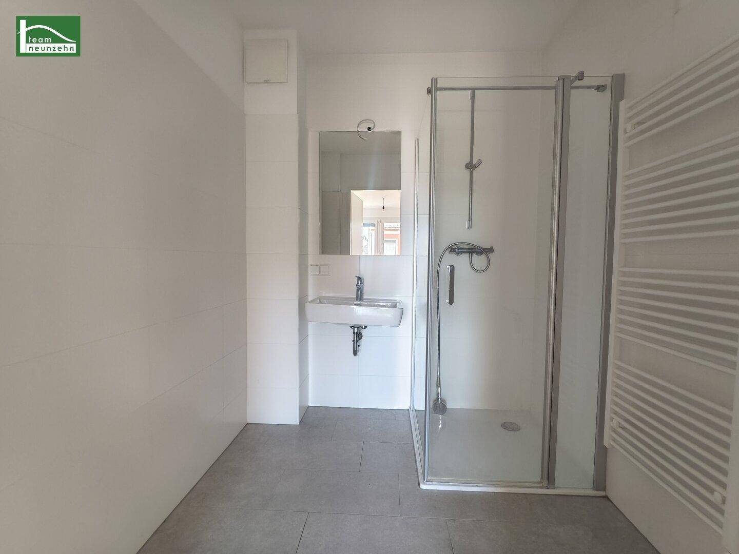 Modernes Badezimmer mit Duschkabine, Waschbecken und beheiztem Handtuchhalter.